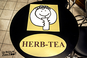logo herb-tea avec au dessus pictogramme, personnage sympatique qui boit sans doute un bubble tea